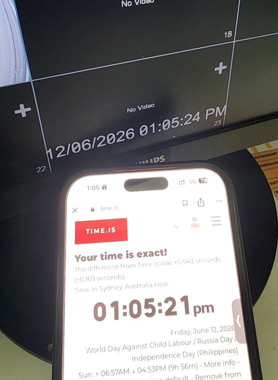 A phone showing the exact time held next to a CCTV monitor, so one photograph captures both clocks
